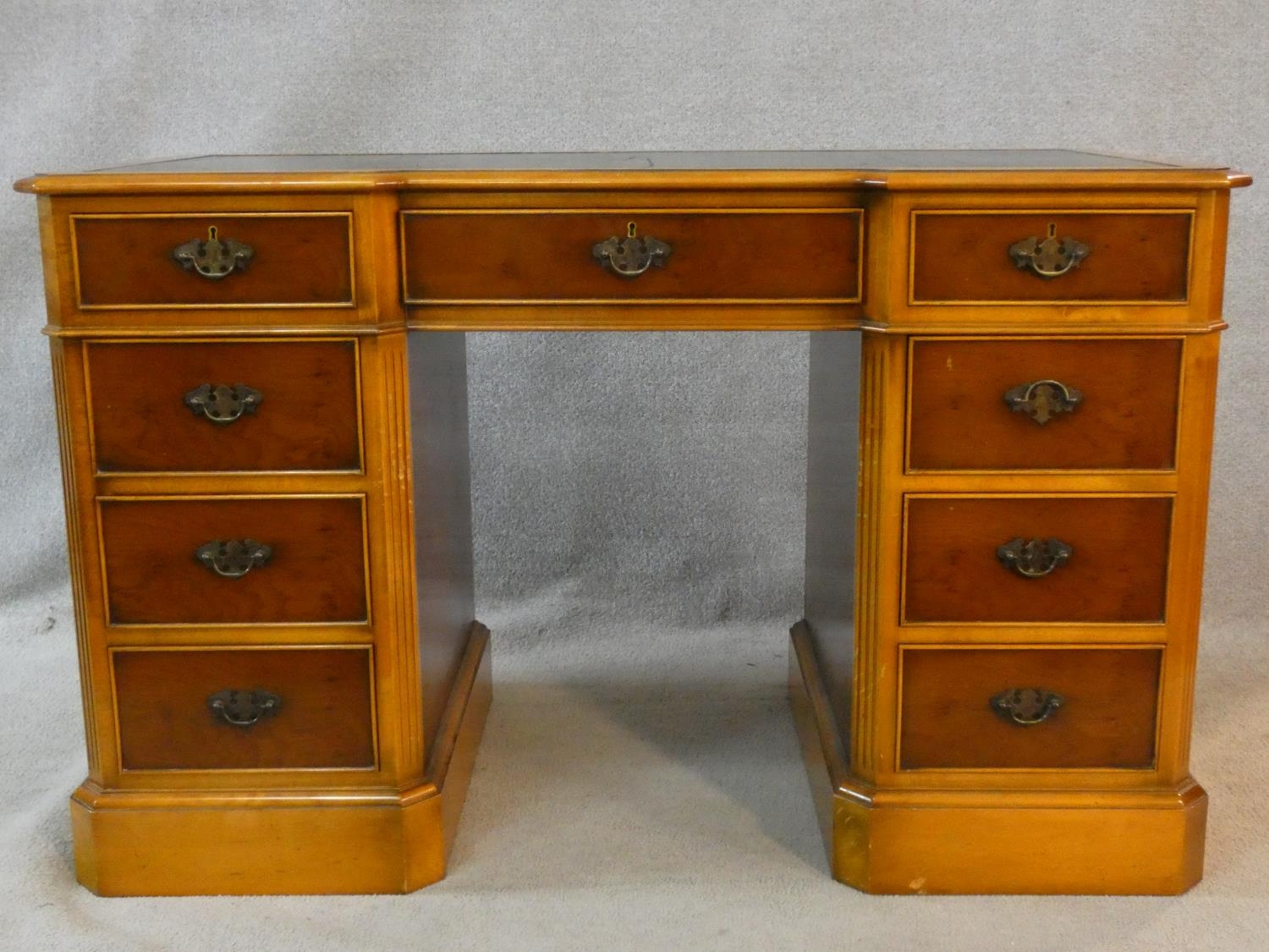 A Georgian style yew pedestal desk with inset tooled leather top above an arrangement of nine