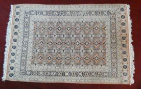 An Eastern woollen rug with repeating lozenge motifs on a beige ground within stylised multiple