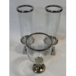 A pair of metal candle stands with glass storm shades and a similar single example with a flared