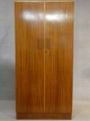 A 1960's teak wardrobe fitted with shelf and hanging space with inset Heal's disc to the inside of