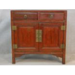 A Chinese hardwood and brass bound side cabinet with frieze drawers above a pair of panel doors on