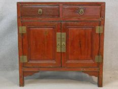 A Chinese hardwood and brass bound side cabinet with frieze drawers above a pair of panel doors on