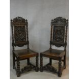 A pair of Continental antique oak hall chairs with crown crestings to the carved backs above panel