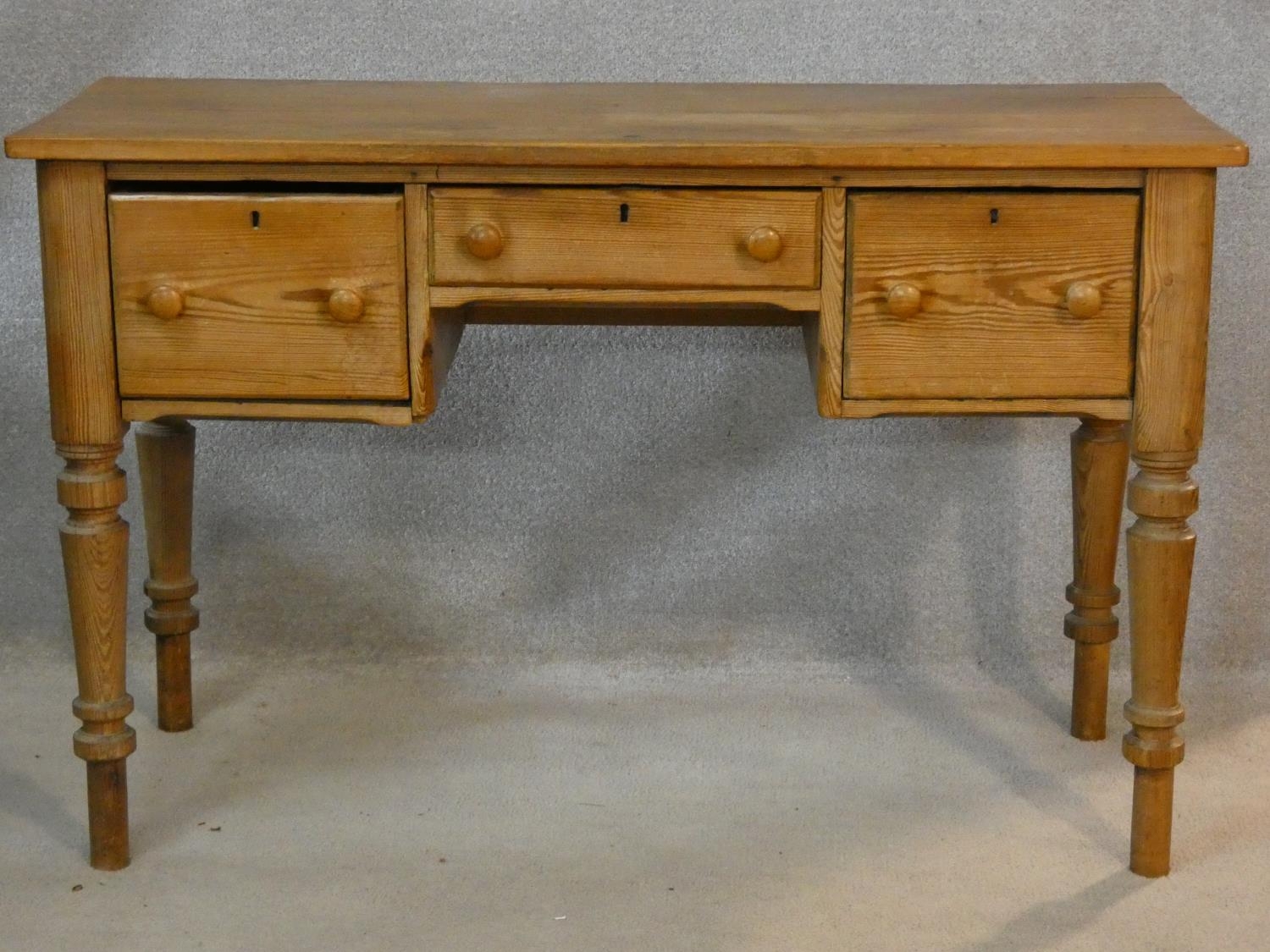 A 19th century pitch pine kneehole writing table with three frieze drawers on turned tapering