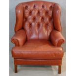 A Georgian style wingback armchair in buttoned leather upholstery on square supports. H.110cm