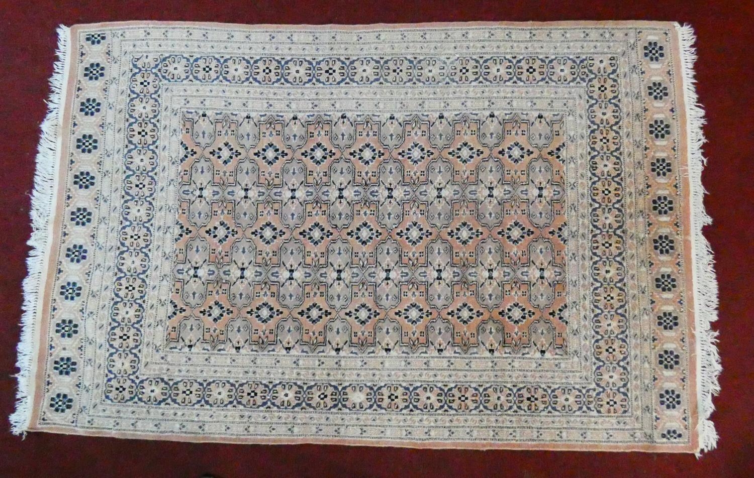 An Eastern woollen rug with repeating lozenge motifs on a beige ground within stylised multiple