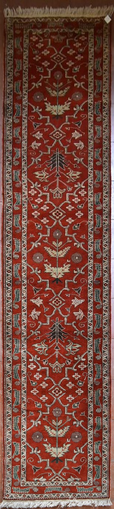 A Moughal style runner with repeating scrolling trellis central design within a border of serrated