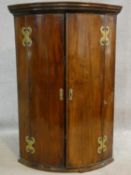 A Georgian mahogany bowfronted corner cabinet with dentil cornice above panel doors with original