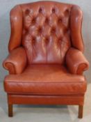 A Georgian style wingback armchair in buttoned leather upholstery on square supports. H.110cm