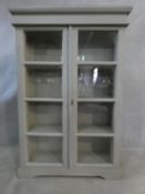 A painted antique style bookcase with glazed doors enclosing shelves on bracket feet. H.135 W.90 D.
