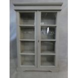 A painted antique style bookcase with glazed doors enclosing shelves on bracket feet. H.135 W.90 D.