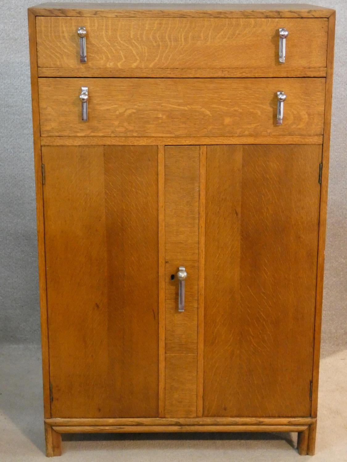 A mid century oak Art Deco style tallboy cabinet with two drawers above panel doors fitted with