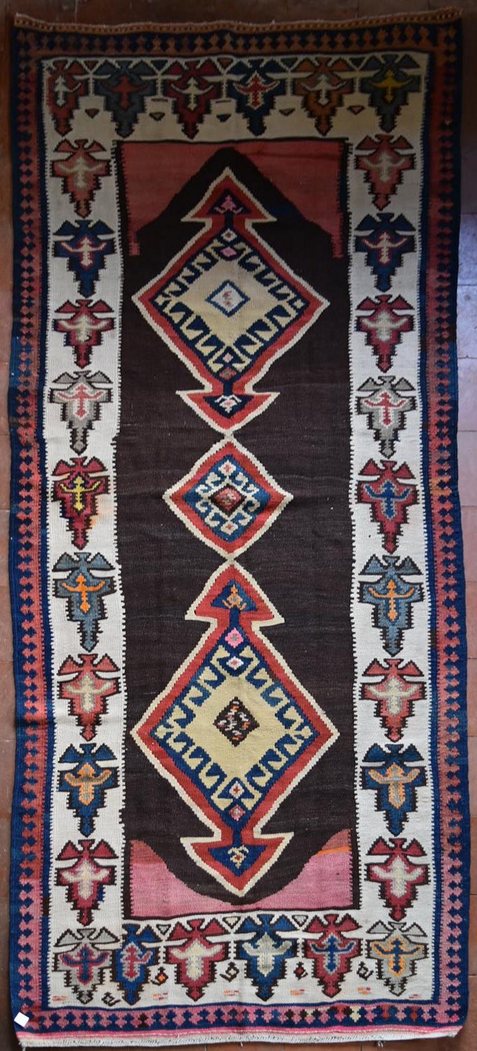 A Persian Kilim with repeating lozenge medallion on umber ground contained by plain spandrels and