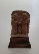 An Indian terracotta relief sculpture of two deities with a young child, mounted on a wooden plinth.