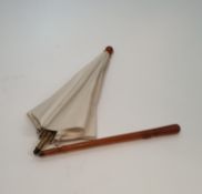 An Oriental antique folding cream silk parasol with an amber resin tapering handle carved with