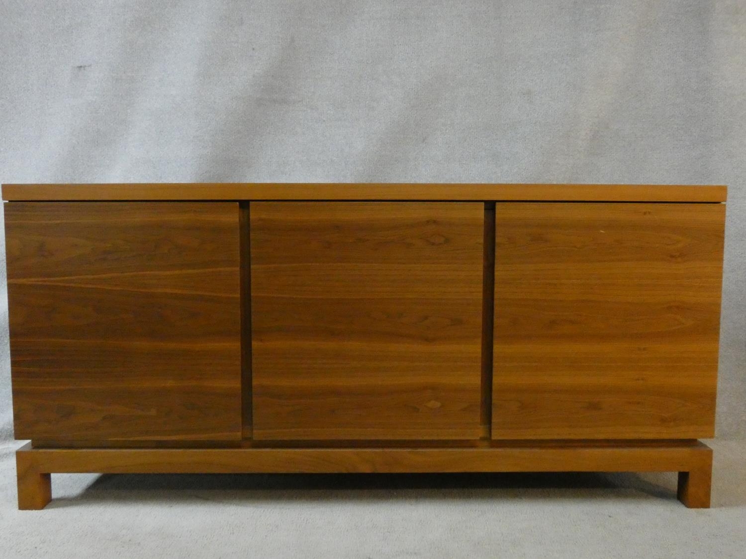 A contemporary teak sideboard with three panel doors on block feet. H.84 W.180 D.40cm