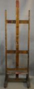 A vintage beech framed full height easel on platform base resting on brass casters. H.175cm