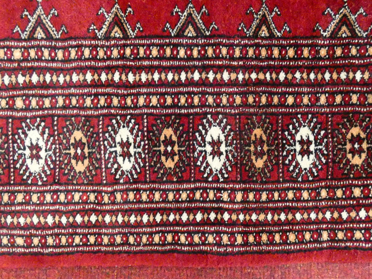 A Bokhara style rug with repeating gul motifs across the madder field enclosed by mutliple geometric - Image 6 of 7