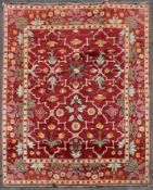 A Moughal design carpet with repeating stylised floral pattern across a madder ground within foliate