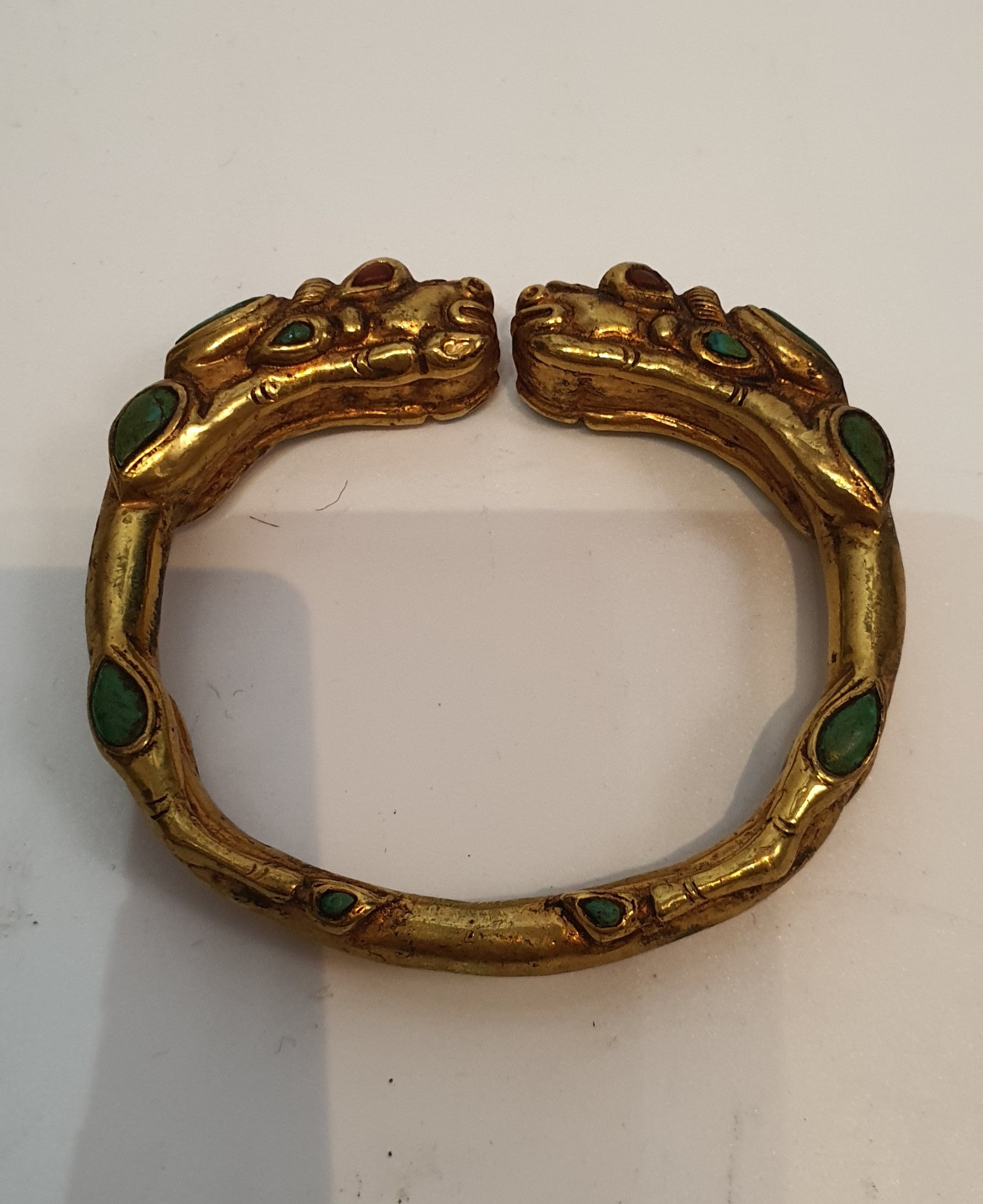 A Tibetan gilded bronze two headed dragon bangle inset with turquoise and red stone cabochons for