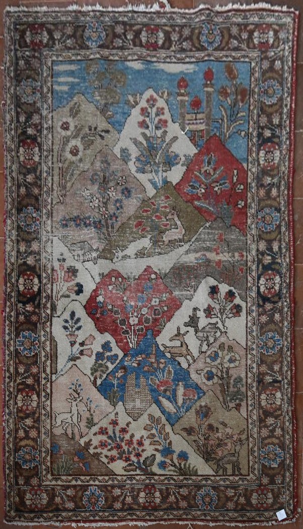 An antique Persian pictorial rug with animals and foliage in a mountain setting within stylised