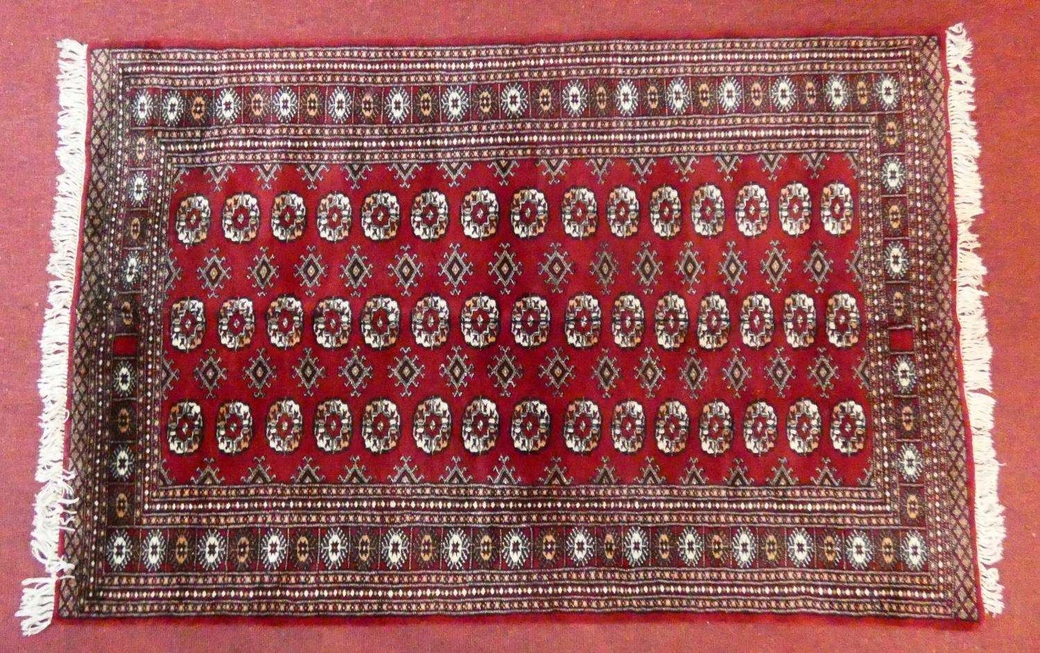 A Bokhara style rug with repeating gul motifs across the madder field enclosed by mutliple geometric