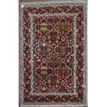 A Moughal design rug with repeating scrolling foliate design on madder field within stylised