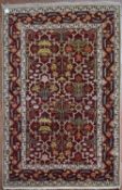 A Moughal design rug with repeating scrolling foliate design on madder field within stylised