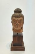 A Chinese terracotta head of buddha with painted details, mounted on a wooden stand. H27cm.
