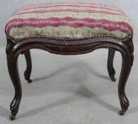 A 19th century mahogany footstool in tapestry upholstery on cabriole supports terminating in brass