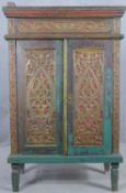 An Eastern polychrome and carved teak cabinet with panel doors enclosing shelves on tapering