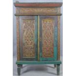An Eastern polychrome and carved teak cabinet with panel doors enclosing shelves on tapering