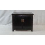 A lacquered Chinese side cabinet with panel doors and brass fittings enclosing a pair of drawers