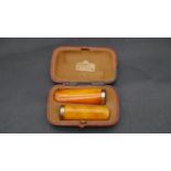 A leather cased pair of 18k gold and amber bakelite cheroot holders. Hallmarked: C.G. Halberg,