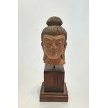 A Chinese terracotta head of buddha with painted details, mounted on a wooden stand. H27cm.