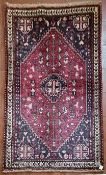 A Persian Kashkai rug with central stepped medallion and highly stylised motifs across a madder