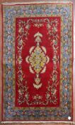 A Persian Qum rug with central medallion decorated with lotus flowers on a burgundy field with