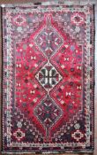 A Persian Shiraz rug with triple pole medallions on a madder ground contained by stylised floral