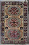 A Turkish Kazak carpet with triple stylised gul medallions on a fawn ground within stylised