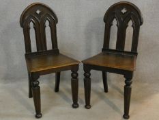 A pair of late 19th century oak hall chairs with Gothic carved and pierced backs above panel seats
