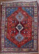 A Persian Shiraz rug with triple pole diamond medallions on a madder ground within sapphire floral