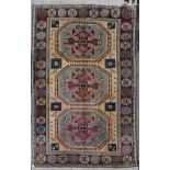 A Turkish Kazak carpet with triple stylised gul medallions on a fawn ground within stylised
