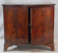 A Georgian style flame mahogany bowfronted side cabinet fitted with crossbanded panel doors on swept