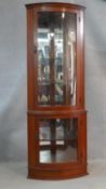 A contemporary mahogany corner cabinet with mirrored back and of bowed outline. H.178 W.65 D.45cm