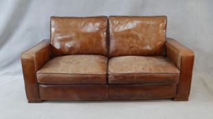A contemporary vintage style sofa in tan leather upholstery on block platform supports. H.75 W.183