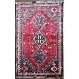 A Persian Shiraz rug with triple pole medallions on a madder ground contained by stylised floral