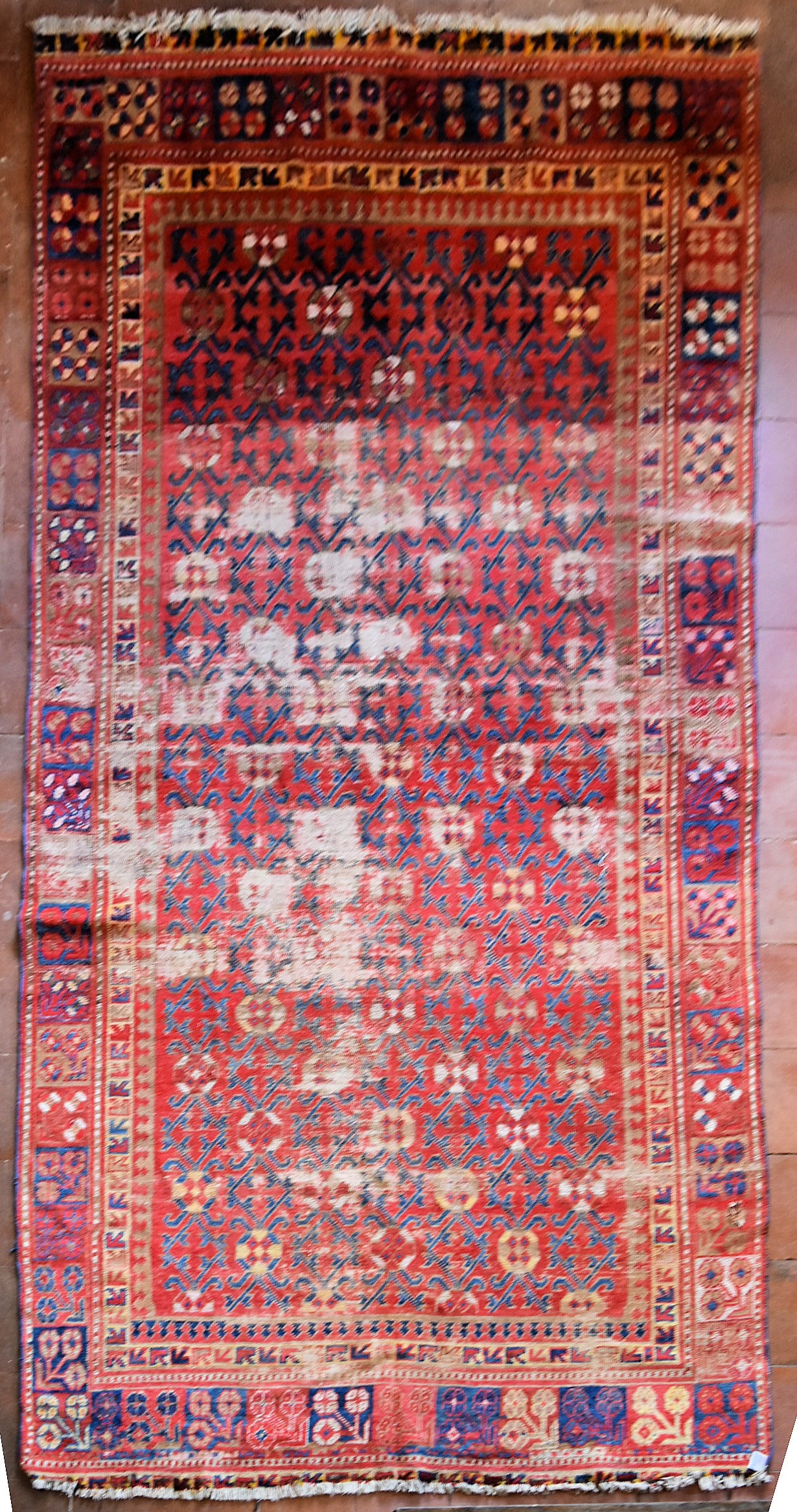 An antique Tabat carpet with repeating gul motifs across the deep red field contained within a