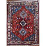 A Persian Shiraz rug with triple pole diamond medallions on a madder ground within sapphire floral