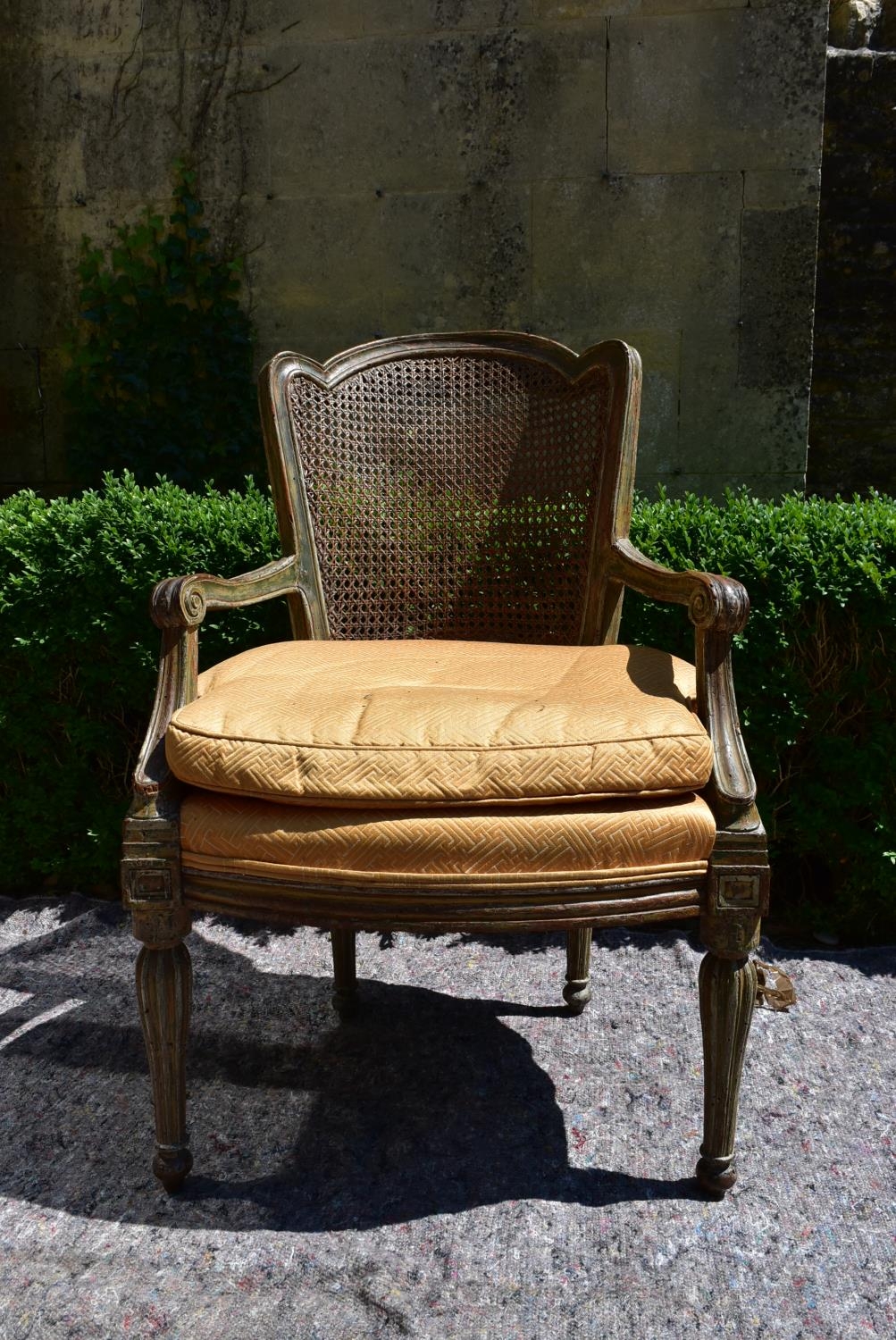 A Continental style painted and caned back armchair with fitted squab cushion raised on shaped