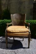 A Continental style painted and caned back armchair with fitted squab cushion raised on shaped
